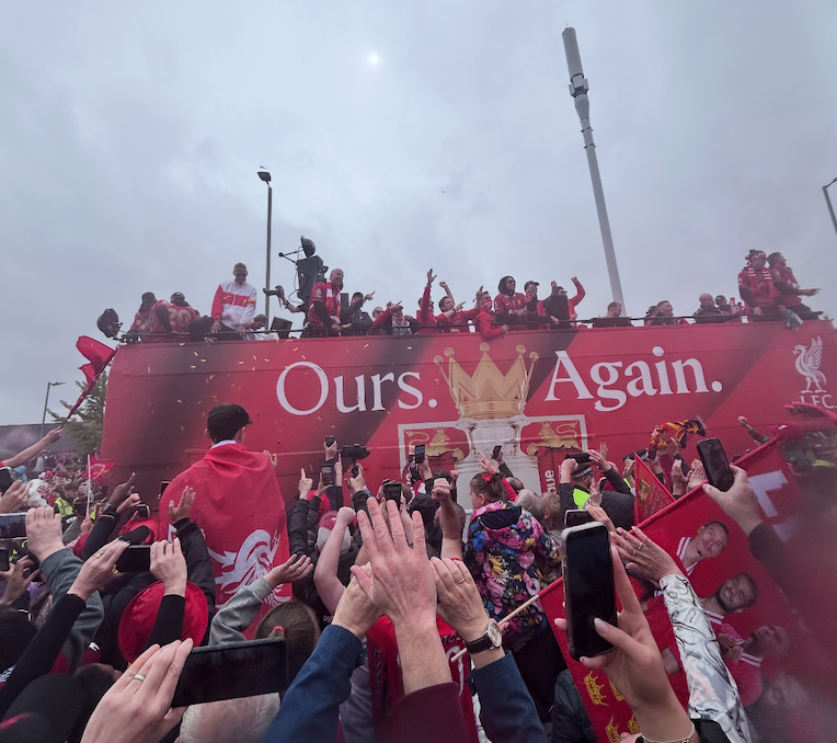 Liverpool football team on an open bus with Premier League trophy with all the fans waving at a street party